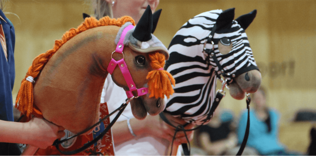 Dwa Hobby Horses z plecionymi grzywami, jeden brązowy z pomarańczową włóczką, a drugi w zebrzy wzór