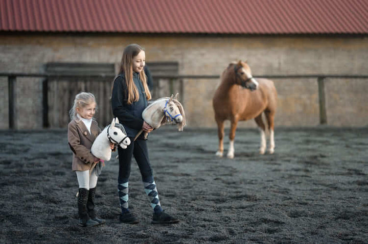 Dwoje dzieci niosących Hobby Horses na zewnętrznej arenie obok kucyka