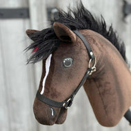 Zbliżenie na Hobby Horse Lucas z czarnym kantarem od Hobby Horse LarDen, brązowego ogiera hanowerskiego z czarną grzywą, białą strzałką na pysku i czarnym kantarem, na rozmytym drewnianym tle.