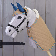 The Hobby Horse LarDen Set Almond Star features a plush hobby horse with a tan quilted blanket, blue ear bonnet, white mane, and black bridle on a wooden stick, shown against a gray wooden wall.