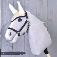 Szary pluszowy Hobby Horse od Hobby Horse LarDen z czerwonymi nausznikami szydełkowanymi Nicol, uzdą i słomkowym kapeluszem, osadzony na drewnianym kiju, na tle drewnianych desek.