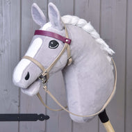 Hobby Horse LarDen przedstawia szarego Hobby Horse z białą grzywą, czarnym okiem i zestawem Bordeaux ze skóry ekologicznej - ogłowie, wodze i martingal — oraz fioletowym naczółkiem i pyskiem w stylu kreskówkowym. Stoi pionowo na drewnianym tle.