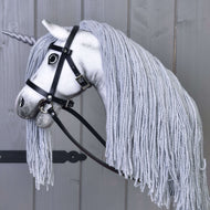 Hobby Horse Jednorożec Silver z Ogłowiem i Kantarem od Hobby Horse LarDen, z białą głową, szarą grzywą z włóczki, jasnoszarym rogiem i czarnym ogłowiem, osadzony na kiju i sfotografowany na drewnianym tle.