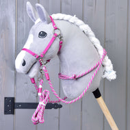 Szary pluszowy Hobby Horse LarDen z białą grzywą jest pokazany z zestawem Zestaw Start Różowy (kantar, cordeo, uwiąz i wodze), osadzony na drewnianym kiju na tle szarej drewnianej ściany.