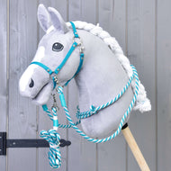 A gray plush hobby horse with a white mane is fitted with the Set Start Turquoise (halter, cordeo, lead rope, and reins) by Hobby Horse LarDen and is displayed against a gray wooden background.