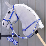 Pluszowy szary hobby horse od Hobby Horse LarDen z zestawem Zestaw Start niebieski: kantarem, smyczą, wodzami i cordeo, z niebiesko-białym uwiązem na drewnianym kiju, stoi przed szarą drewnianą ścianą.