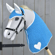Hobby Horse LarDen „Zestaw Mystery” przedstawia szarego konia z niebieskim teksturowanym okryciem przypominającym derkę, białymi uszami, białym sercem na boku, czarną uzdą, grubą białą grzywą i osadzonego na kiju, na tle drewna.