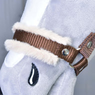 Zbliżenie na „Kantar brązowy z futerkiem” Hobby Horse LarDen, dodatek do jasnoszarego pluszowego Hobby Horse z brązowym kantarem, białym wykończeniem ze sztucznego futerka, metalowymi nitami i przyszytym czarnym detalem w kształcie łzy.