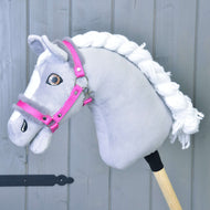 Hobby Horse LarDen „Kantar różowy z futerkiem” pokazany na szarym Hobby Horse z białą włóczkową grzywą, białymi znaczeniami na pysku i osadzony na drewnianym kiju, na tle szarych drewnianych desek.