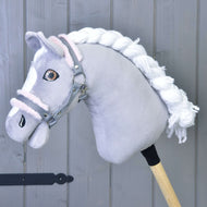 Hobby Horse LarDen „Kantar szary z różowym futerkiem” przedstawia szarego pluszowego konia z białą grzywą i szarym kantarem, przymocowanego do drewnianego kija, na tle szarych drewnianych paneli.
