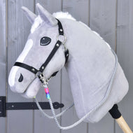 The Hobby Horse LarDen Reins Manhattan features a gray hobby horse with a white mane, black halter, handmade reins, and a wooden stick, shown against a gray wooden wall.