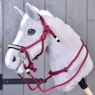 The Hobby Horse LarDen Rope set Burgundy features a gray plush hobby horse with a white mane, black nose, and burgundy rope halter, mounted on a wooden stick and displayed against a gray wooden wall.