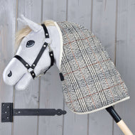 Szary pluszowy Hobby Horse od Hobby Horse LarDen ma czarną uzdę i derkę stajenną Fine Check, jest osadzony na drewnianym kiju i pokazany na tle jasnoszarej drewnianej ściany.