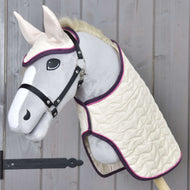 Hobby Horse LarDen Zestaw Supreme Crema na pluszowym Hobby Horse z szarą głową, białym pyskiem i uszami, ubranym w pikowaną kremową derkę i pasujące nauszniki z fioletowym wykończeniem, pokazany na drewnianej ścianie.