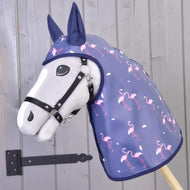 Płaszcz przeciwdeszczowy Flamingo od Hobby Horse LarDen, czyli szary Hobby Horse w granatowym kapturze przeciwdeszczowym z różowymi flamingami, ustawiony jest przed drewnianą ścianą z czarnym metalowym zawiasem.