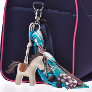 A close-up of a navy blue bag with pink trim, featuring the Hobby Horse LarDen Keychain Horse Grey and a colorful patterned scarf tied in a bow on one of the bag’s metal rings.