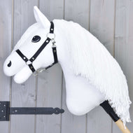 The Hobby Horse Lady with Black Halter by Hobby Horse LarDen features a white horse head with a long yarn mane, black halter, and bold black eyes on a wooden stick, displayed against a gray wooden background.