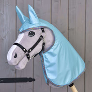 Szary Hobby Horse Hobby Horse LarDen z czarną uzdą, dużymi filcowymi oczami oraz kapturem Płaszcz przeciwdeszczowy Jasnoniebieski z dopasowanymi uszami, na tle drewnianej ściany.
