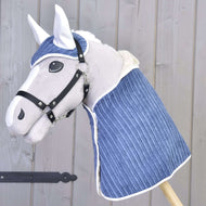 Hobby Horse LarDen Zestaw Manchester Śliwka przedstawia pluszowego Hobby Horse z białym pyskiem, czarnym ogłowiem i niebieskim pikowanym okryciem oraz pasującymi nausznikami, na tle jasnej drewnianej ściany.