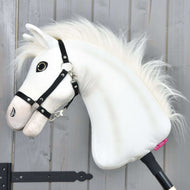 Hobby Horse LarDen Hobby Horse Nexus z czarnym kantarem ma białego pluszowego konia sportowego z puszystą grzywą, dużym guziczkowym okiem i czarnym kantarem — idealny dla każdego miłośnika. Zdjęcie na tle szarej drewnianej ściany.