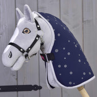 Szary pluszowy Hobby Horse od Hobby Horse LarDen z czarną uzdą i derką stajenną Night Sky, osadzony na drewnianym kiju na tle jasnej drewnianej ściany.