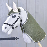 The Set Olivetti by Hobby Horse LarDen is a gray hobby horse with a green quilted blanket and bridle, black halter, white ears, and stylish accessories, shown against a light gray wooden wall.