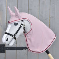 Szary Hobby Horse LarDen na drewnianym patyku nosi czarną uzdę i płaszcz przeciwdeszczowy Veloria w kolorze różowym na głowie i szyi, ustawiony na tle jasnego drewnianego płotu.