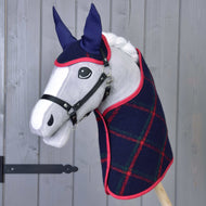 The Hobby Horse LarDen "Set Tartan" plush hobby horse features a gray face, black bridle, blue ears, and a navy plaid blanket with red trim, posed before a gray wooden wall.