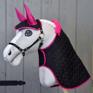 Hobby Horse LarDen „Zestaw Termo Czarny z Futrem” przedstawia pluszowego Hobby Horse z białym pyskiem, różowymi uszami, czarnym ogłowiem i splecioną białą grzywą, pokazany na drewnianym tle. Ma czarną pikowaną derkę z jaskraworóżowym obszyciem.