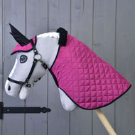 Pluszowy Hobby Horse od Hobby Horse LarDen stoi na drewnianym kiju, ma biały pysk, czarne ogłowie i nosi derkę oraz nauszniki Zestaw Termo Różowy na tle szarej ściany — urocza dekoracja jeździecka.