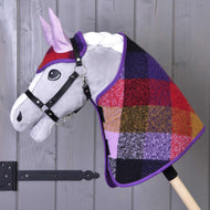 Zestaw Jesienny Kratka 2 od Hobby Horse LarDen przedstawia pluszowego Hobby Horse z szarym pyskiem, czarnym ogłowiem i kolorową patchworkową kratą na szyi, osadzonego na drewnianym kiju, pokazany na tle drewnianej ściany.