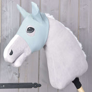 Hobby Horse LarDen „Hobby Horse Mask Spiky” przedstawia pluszowego szarego konia z jasnoniebieską uzdą, białą grzywą i maską ochronną na drewnianym kiju, pokazanym na tle jasnych drewnianych desek.