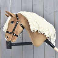 The Hobby Horse LarDen Hobby Horse Smart with Black Halter, featuring a cream yarn mane and wooden stick, is displayed on a wooden wall with vertical gray panels.