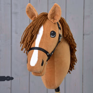 Hobby Horse Wendy z czarnym kantarem od Hobby Horse LarDen ma brązową pluszową głowę, zaplecioną brązową grzywę z włóczki, biały pasek na pysku i czarny kantar, inspirowany kasztanowatą klaczą, pokazany na tle szarego drewna.