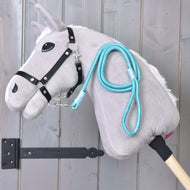 Hobby Horse - sznurkowy pasek Atlantis Hobby Horse LarDen z szarą pluszową głową, czarną uzdą i niebieską smyczą sznurkową, osadzony na drewnianym kiju i pokazany na tle pionowych drewnianych desek.