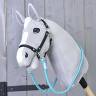 Hobby Horse LarDen Reins Atlantis to szary pluszowy Hobby Horse z czarną uzdą i niebieskimi wodzami ze sznurka polipropylenowego na drewnianym kiju, pokazany przed rustykalną drewnianą ścianą.