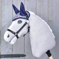 Czapka na uszy Flower od Hobby Horse LarDen na pluszowym Hobby Horse z jasnoszarą głową, czarną uzdą oraz błyszczącą fioletowo-srebrną czapką na uszy zapewniającą ochronę przed owadami, pokazana na drewnianym tle.