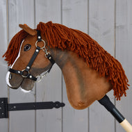 Hobby Horse Cooper z czarnym kantarem od Hobby Horse LarDen ma brązową materiałową głowę z grzywą z włóczki, białą łysinę na nosie i jest osadzony na drewnianym kiju. Stylizowany na eleganckiego konia sportowego, idealnie nadaje się do kreatywnej zabawy w ujeżdżenie i jest sfotografowany na tle szarego drewnianego tła.