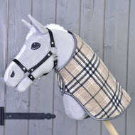 Hobby Horse LarDen „Blanket Cremo England” to szary Hobby Horse z czarnym kantarem i beżowym okryciem w kratę, z nausznikiem zapewniającym ochronę przed owadami, osadzony na drewnianym kiju na tle szarej drewnianej ściany.