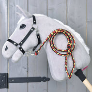 Hobby Horse LarDen „Hobby Horse - lina w paski Flag” to szary pluszowy Hobby Horse z korpusem na kiju, białą grzywą, czarną uzdą i plecioną smyczą w kolorach czerwonym, żółtym i czarnym, pokazany na drewnianym tle.