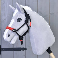 The Hobby Horse LarDen Rope halter Spark is a gray hobby horse toy with a white mane and black-and-red rope halter, mounted on a wooden stick and set in front of a gray wooden wall.