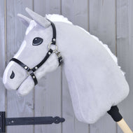 Szary pluszowy Hobby Horse od Hobby Horse LarDen z białą grzywą i kantarem Kantar - czarna skóra ekologiczna, osadzony na drewnianym kiju na tle drewnianych paneli.