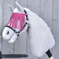 Pluszowy Hobby Horse LarDen nosi Kantar czarny z różowymi frędzlami i stoi na tle szarego drewnianego tła, z białą sierścią i stylowym naczółkiem z różowymi frędzlami.