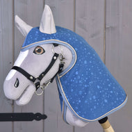 Płaszcz przeciwdeszczowy Dolly (softshell) od Hobby Horse LarDen przedstawia szarego hobby horse z niebieską derką we wzór kropli wody i uzdą na drewnianym kiju — idealny do zabawy w każdą pogodę na tle rustykalnych drewnianych desek.