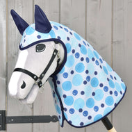 Hobby Horse LarDen Raincoat Bubbles z białą twarzą, czarną uzdą, niebieskimi uszami i jasnoniebieską nakładką w kropki z akcesoriami na każdą pogodę, na drewnianym kiju, pokazany przed drewnianą ścianą.