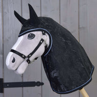 Pluszowa głowa konia na drewnianym kiju nosi Płaszcz przeciwdeszczowy Silver Stone Hobby Horse LarDen z osłonami na uszy i kantarem, stojąc przed drzwiami z drewnianych paneli.