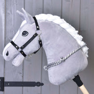 Cordeo w srebrne paski Hobby Horse LarDen na pluszowym szarym Hobby Horse z białą grzywą, czarnym ogłowiem i ręcznie wykonanym szaro-białym cordeo, pokazane na tle drewnianych desek z czarnymi metalowymi okuciami.