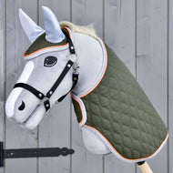 Hobby Horse LarDen Zestaw Moos przedstawia szarego Hobby Horse z czarną uzdą, zieloną pikowaną derką i jasnoniebieskim nausznikiem na drewnianym kiju, pokazane na tle szarej drewnianej ściany.