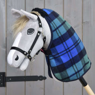 Hobby Horse LarDen z szarą materiałową głową, czarnym ogłowiem, jasną grzywą, malowanym okiem i nozdrzem, nosi derkę Derka Stajenna Perth w niebiesko-zieloną kratę. Stoi na drewnianym tle.