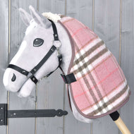 Hobby Horse LarDen „Stable Blanket Lady” to szary pluszowy Hobby Horse z różowo-brązową derką w kratę i czarną uzdą na drewnianym kiju, na tle szarego drewnianego tła.
